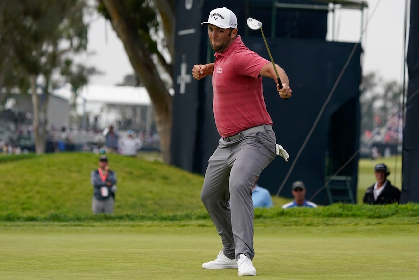 Jon Rahm punches the air while holding his putter at the US Open golf.