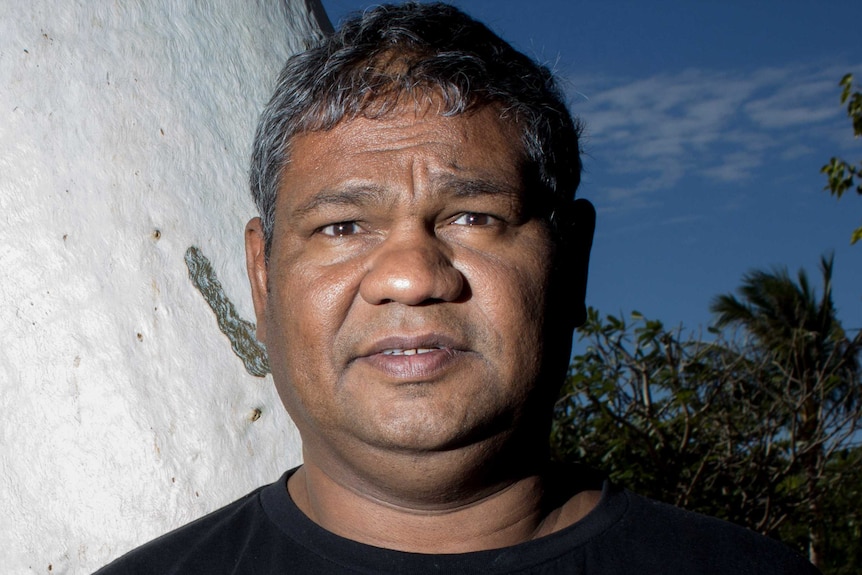 An Indigenous man in a black T-shift looks at the camera 