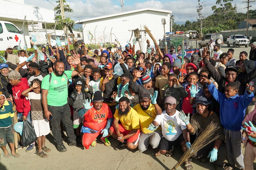 The group holds their hands, shovels and brooms in the air, waving at the camera.