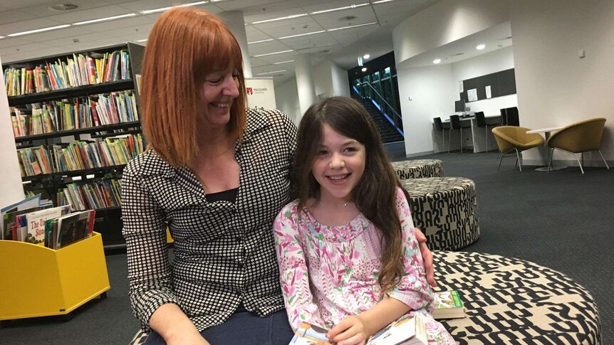A mother and daughter reading at a library.