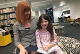 A mother and daughter reading at a library.