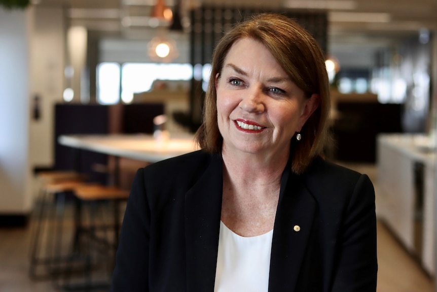 Woman wearing white t-shirt and black blazer sits and smiles for the camera.