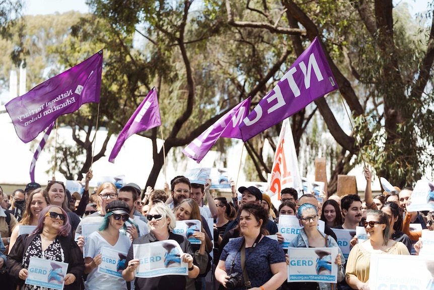 Large group of people holding signs and flags with trees in background