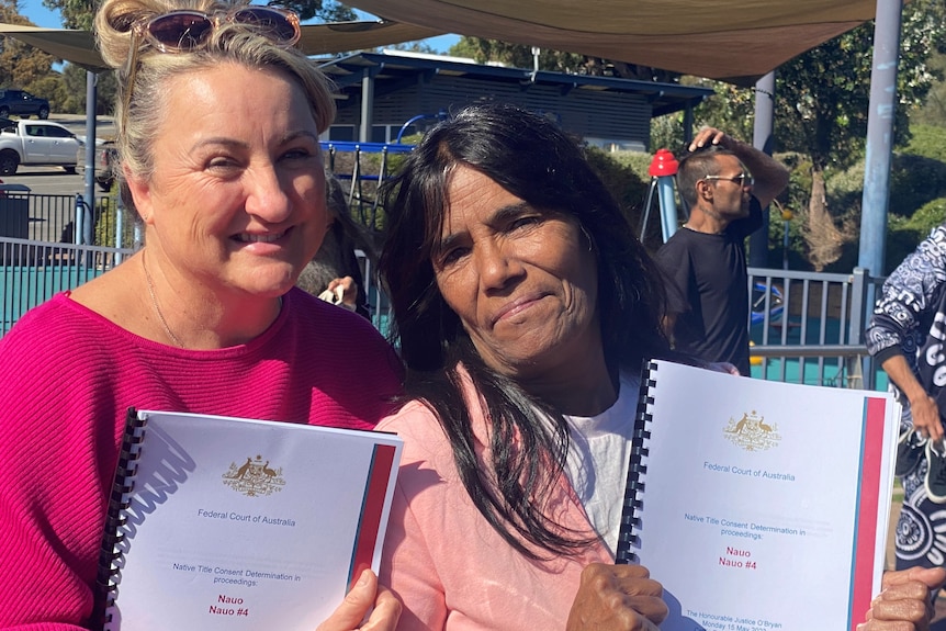 Head and shoulders of white woman and Indigenous woman both holding documents and smiling.