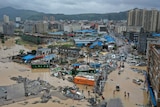 An aerial image shows a Chinese town with typhoon debris and floodwaters. Mountains are seen in the distance.