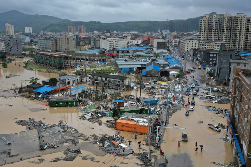 An aerial image shows a Chinese town with typhoon debris and floodwaters. Mountains are seen in the distance.