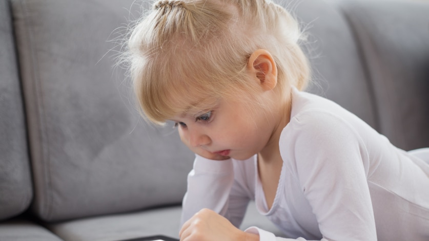 Little girl lying on a lounge looking at a tablet computer
