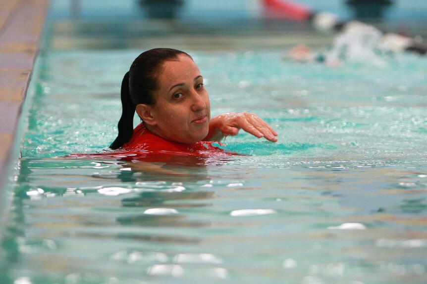 A woman with a red rash vest on in an indoor swimming pool