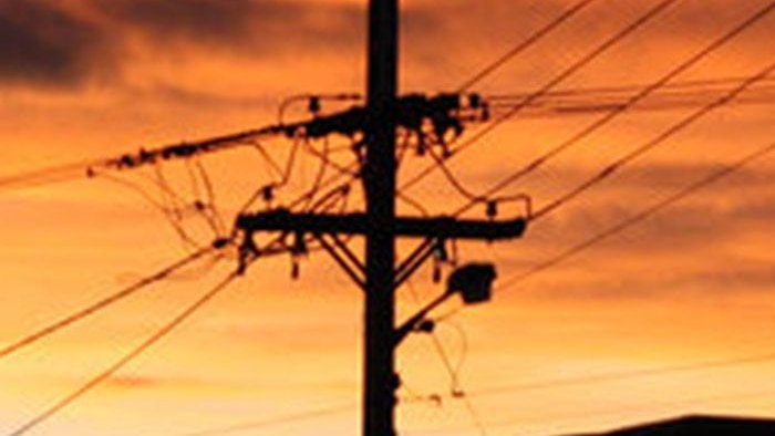 Silhouette of a power pole with many lines with red sunrise behind