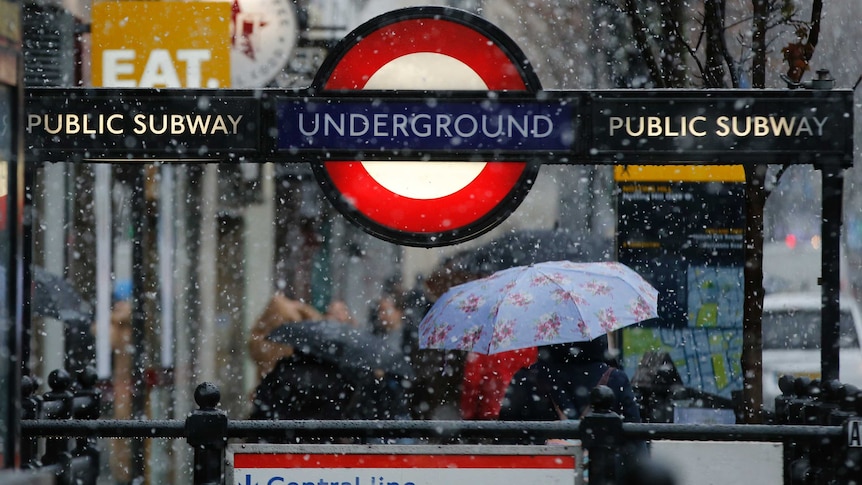 An underground station sign in London with snow falling.