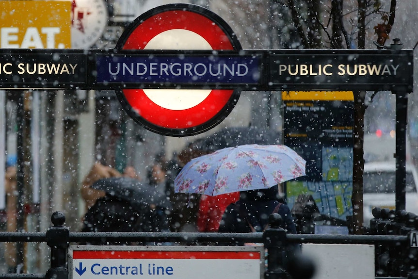 An underground station sign in London with snow falling.