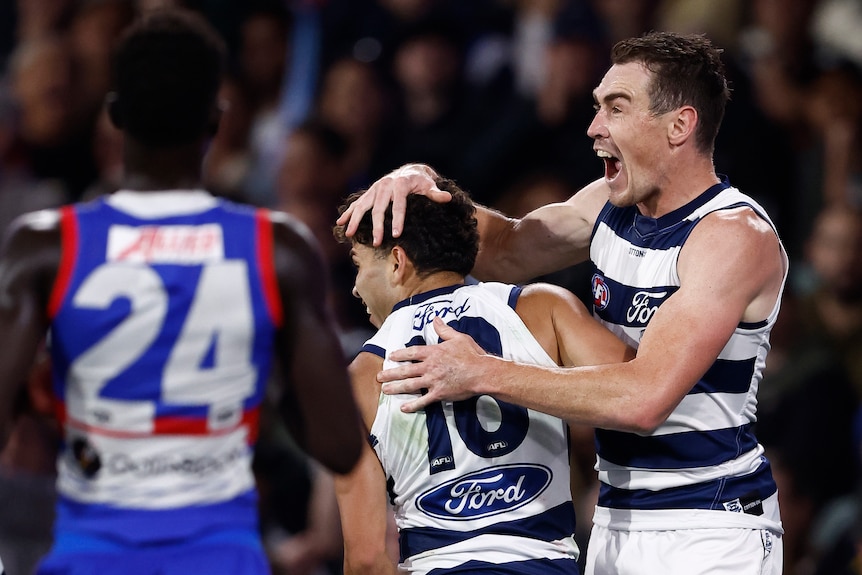 Two Geelong players celebrate, with one rubbing the other's head after a goal.