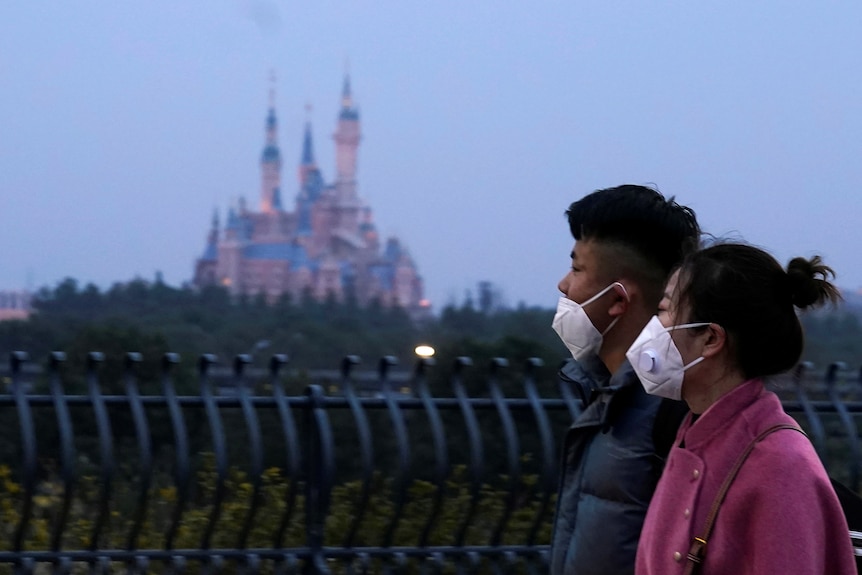 背景中的上海迪士尼城堡塔楼，前景中一对戴着口罩的夫妇失焦