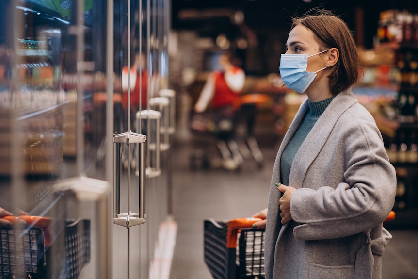 A woman wearing face mask shopping at a grocery store.