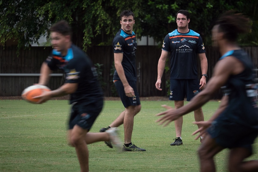 Footballers running drills while coach watches on