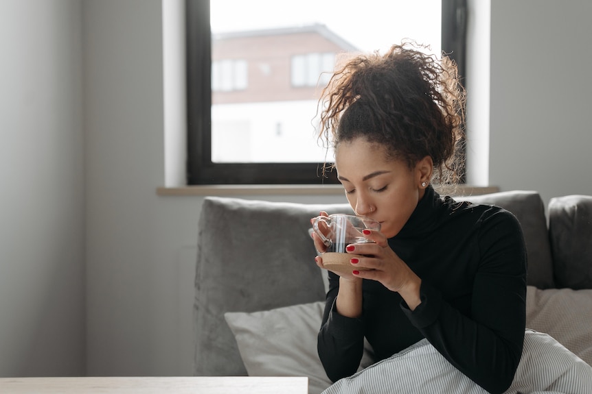 A woman sitting on the coach while drinking tea in a glass cup