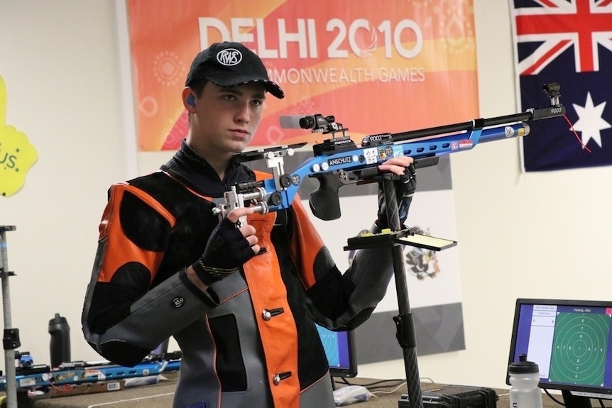 Alex Hoburg holds an air rifle while wearing his competitive garb