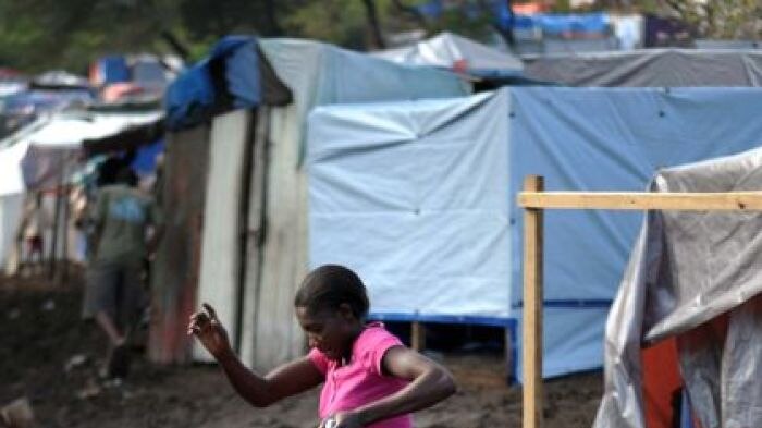 A Haitian woman jumps over a muddy path between tents at a camp in Port-au-Prince