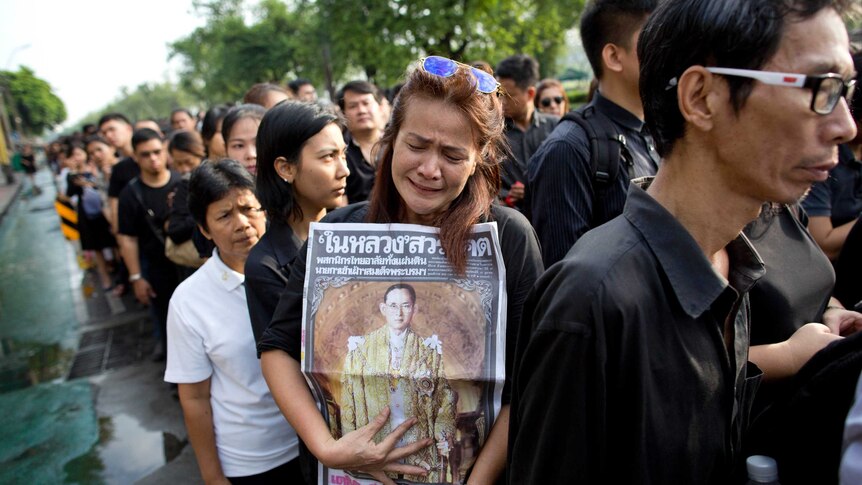 A Thai woman weeps as she holds on to a portrait of Thai King Bhumibol Adulyadej in a line to offer condolences.