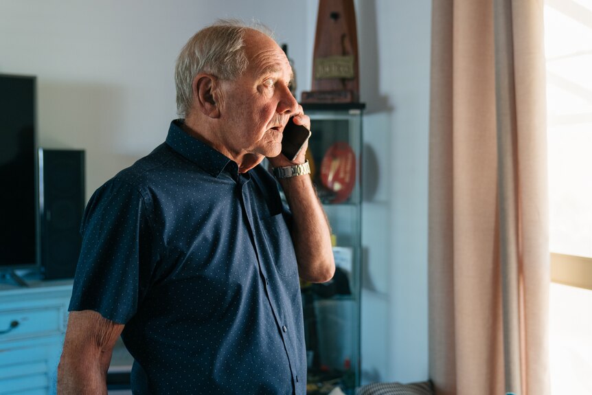 A man wearing a blue shirt speaks on a mobile phone.