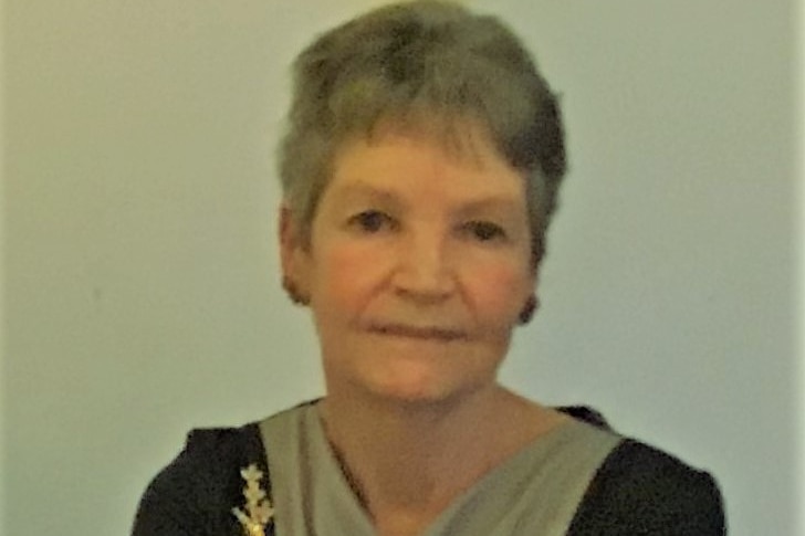 an older woman in a room with grey walls smiling without using teeth