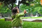 Little girl playing with bubbles in the backyard to depict cheap, simple ways to make your home fun for children