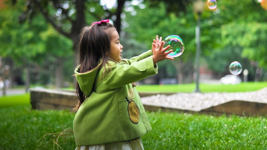 Little girl playing with bubbles in the backyard to depict cheap, simple ways to make your home fun for children