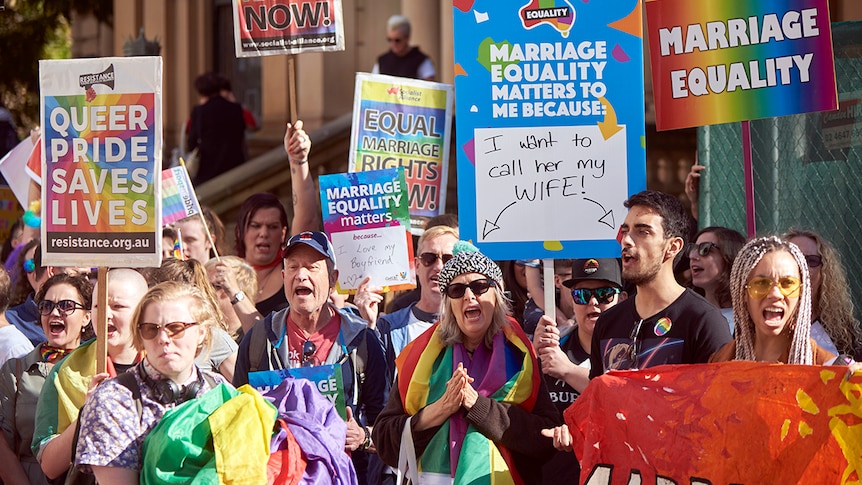 Protesters hold rainbow-coloured signs and flags calling for equal marriage rights during a March in Sydney.