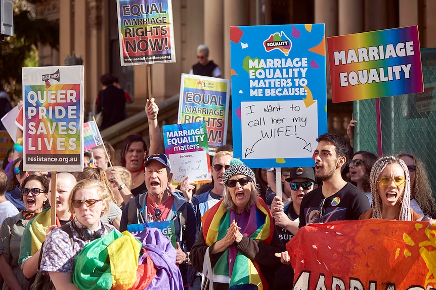 Protesters hold rainbow-coloured signs and flags calling for equal marriage rights during a March in Sydney.