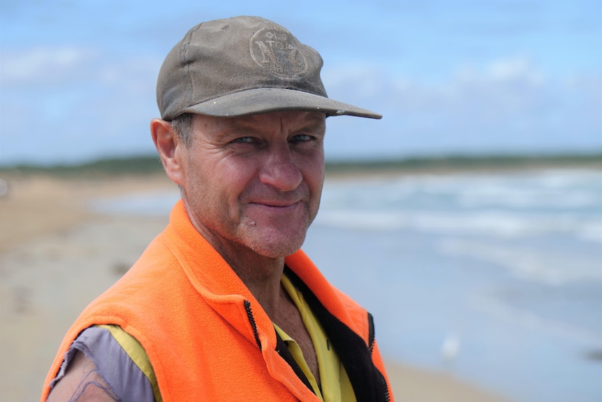 Portrait of a man in building workwear and a faded cap on the beach