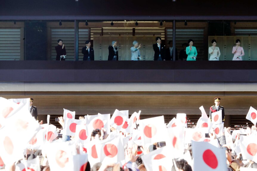 A sea of Japanese flags flutter as crowds wave to greet the Japanese imperial family behind a bullet-proof balcony.