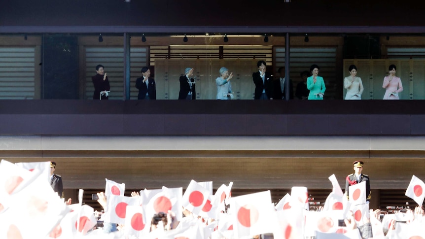 A sea of Japanese flags flutter as crowds wave to greet the Japanese imperial family behind a bullet-proof balcony.