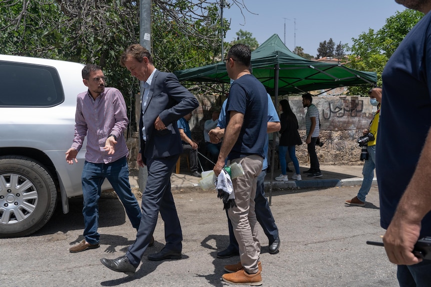 A European man in a suit walks down a street surrounded by several Arab men