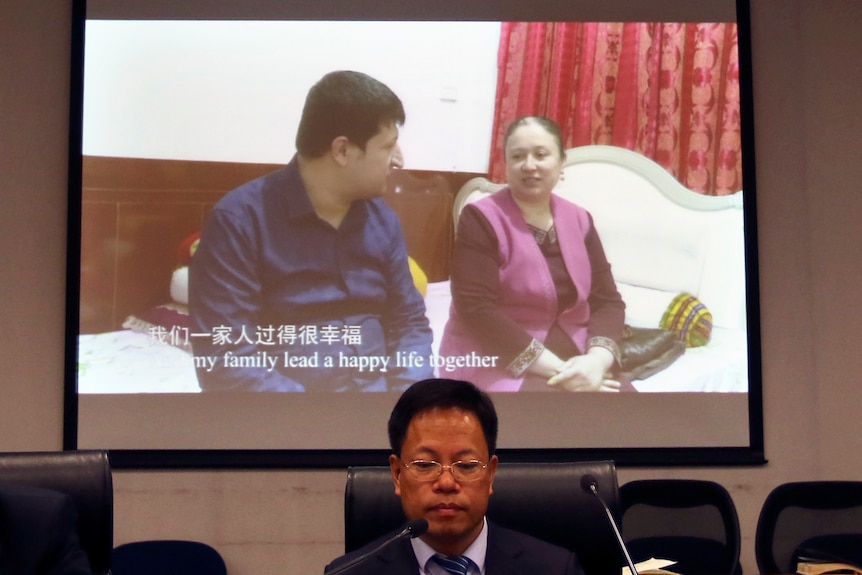 A man sits in front of a screen showing a Uyghur couple living a 'happy life'