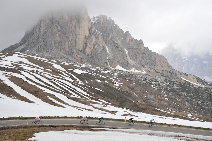 Riders cycle past a misty mountain with snow on it
