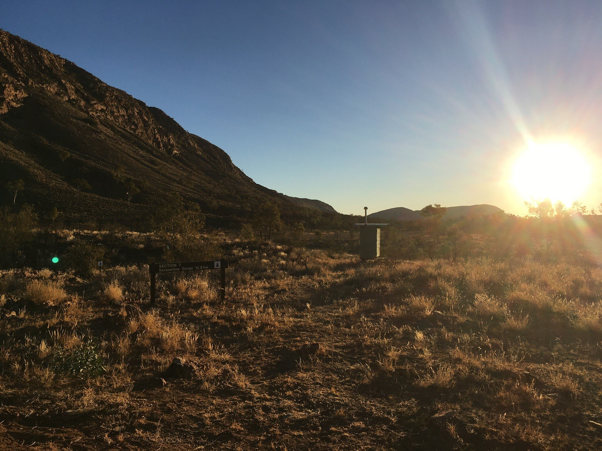 Sunrise over a small cylindrical structure in the distance.  Hill to the left of image 