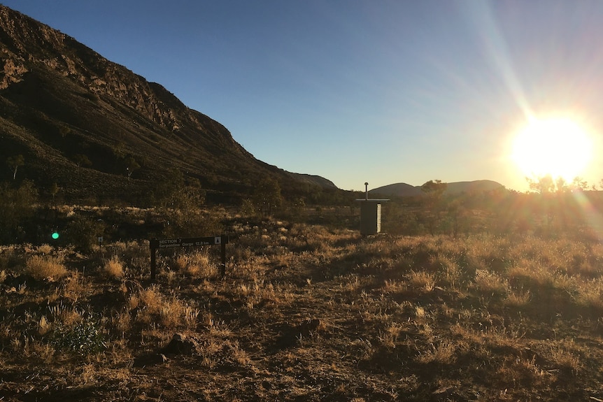 Sunrise over a small cylindrical structure in the distance.  Hill to the left of image 