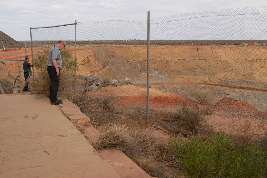 Two men look through a fence over an open mine pit.