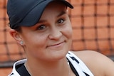 Ash Barty smiles and claps her hand against her racquet