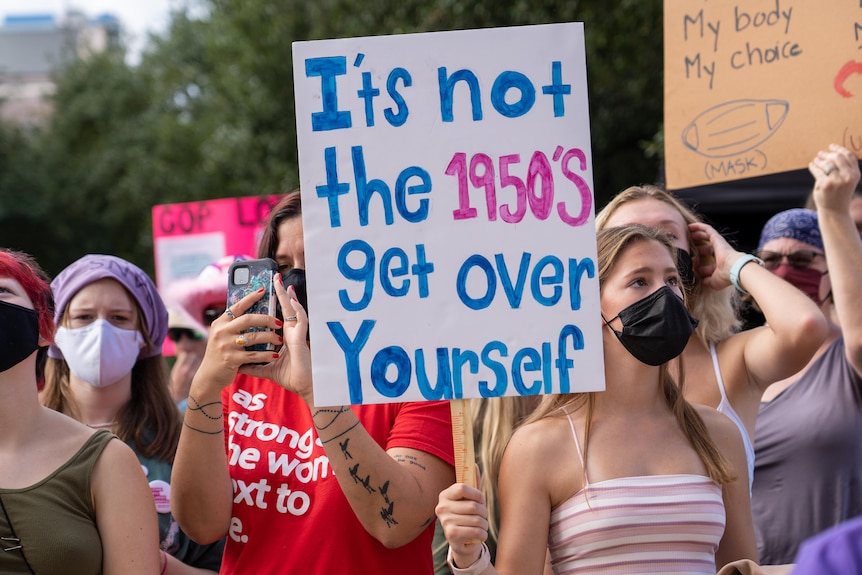 Women at a protest - a sign reads, 'It's not the 1950s, get over yourself'.