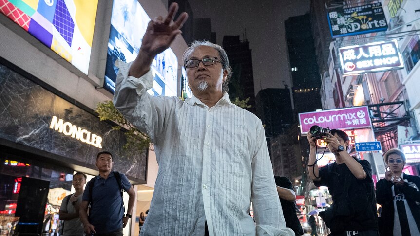 Man in white shirt holds his hand up high.