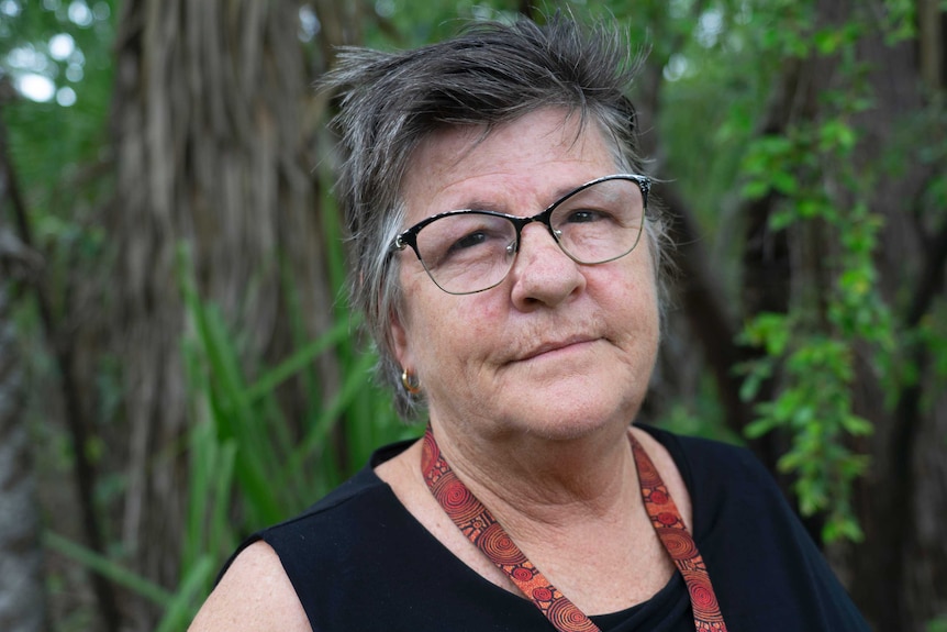 Traditional owner Helen Bishop, wearing glasses, looks towards the camera, with green foliage in the background.
