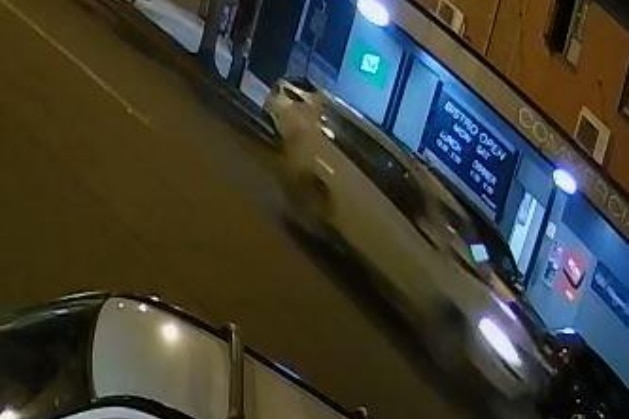 a blurry screenshot of cctv footage of a white vehicle driving down a street