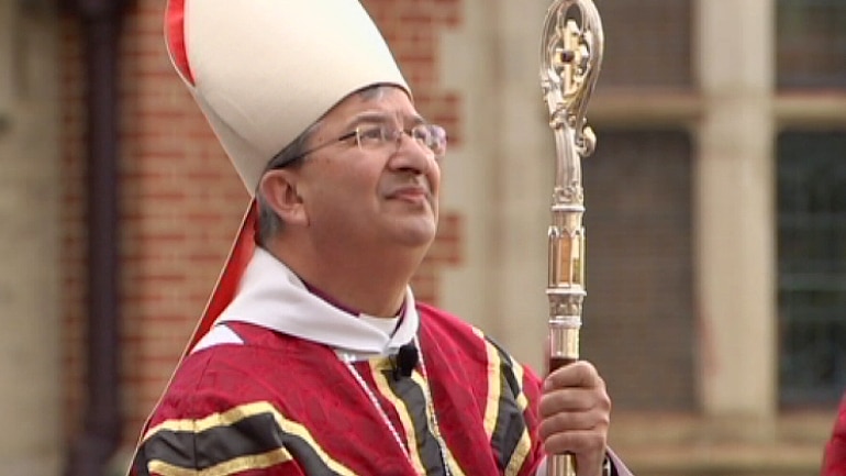 A man with grey hair and glasses wearing elaborate bishop's robes and holding a staff.