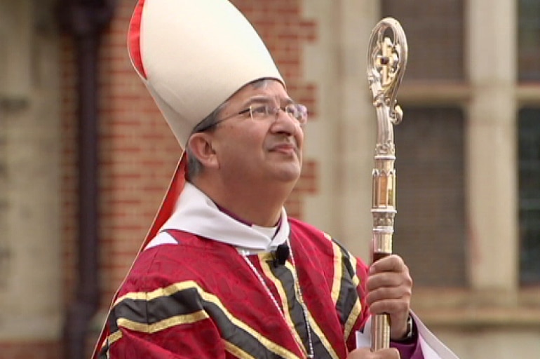 A man with grey hair and glasses wearing elaborate bishop's robes and holding a staff.