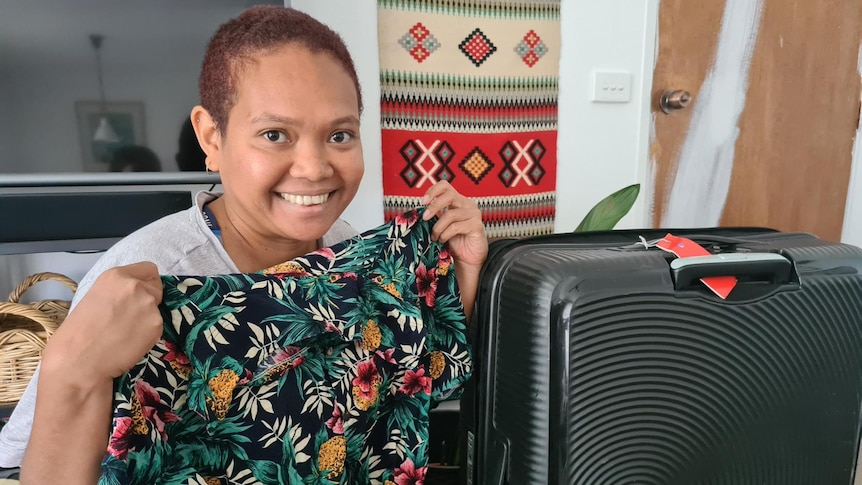 Angela Lawrence holds up a Hawaiian shirt, next to a suitcase