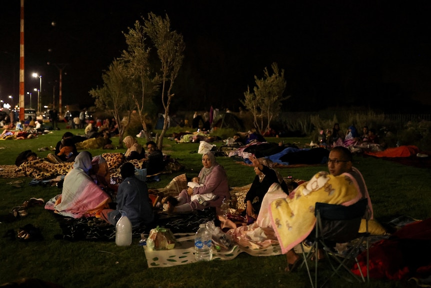 Dozens of people sitting on blankets outside on the grasslate at night