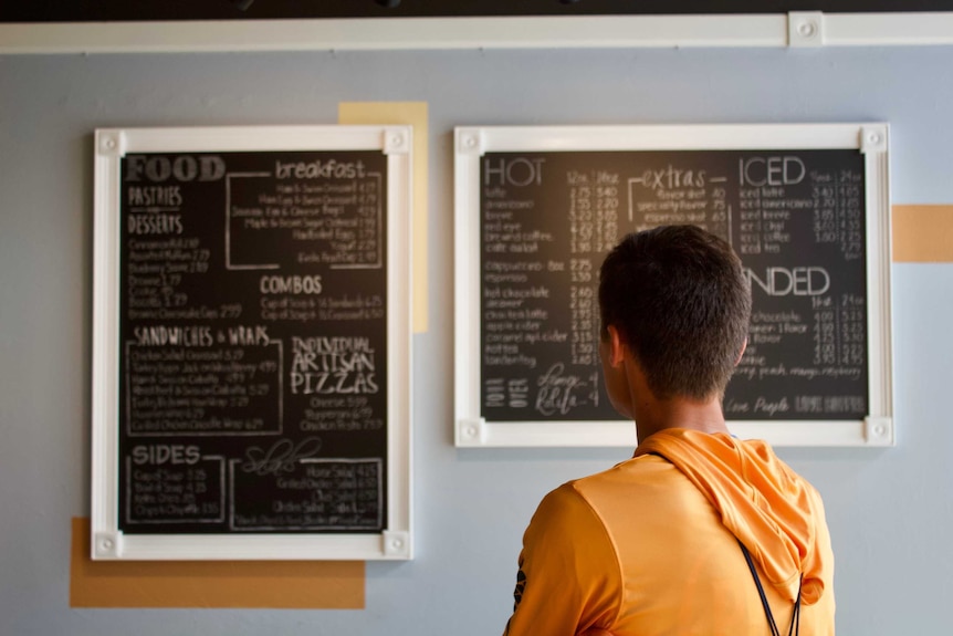 A man looks at a restaurant menu painted onto blackboards, trying to choose a meal.