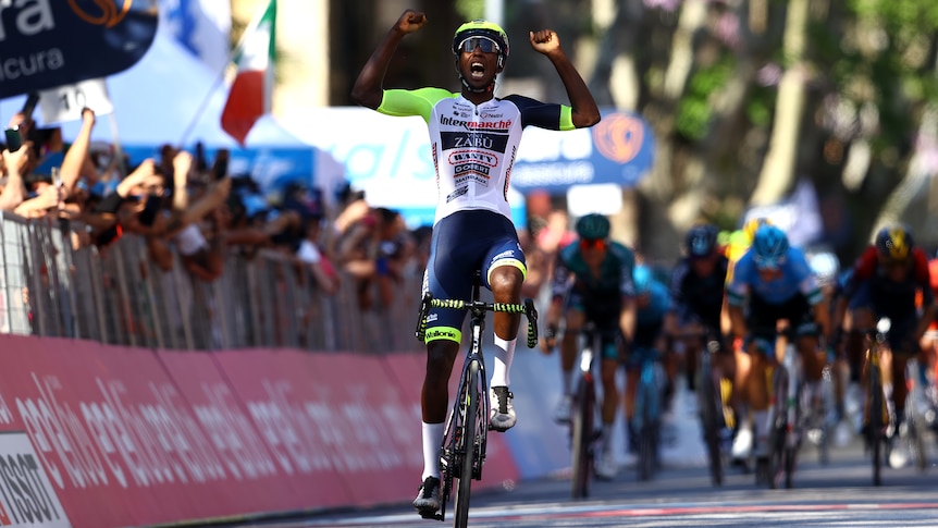 An African professional cyclist raises his arms in triumph as he crosses the finish line on a stage of the Giro D'Italia.