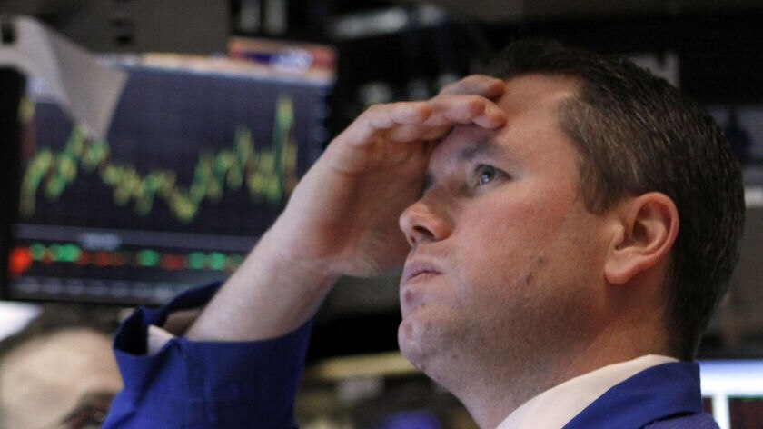 A trader, looking worried works on the floor of the New York Stock Exchange, with a graph on a scree